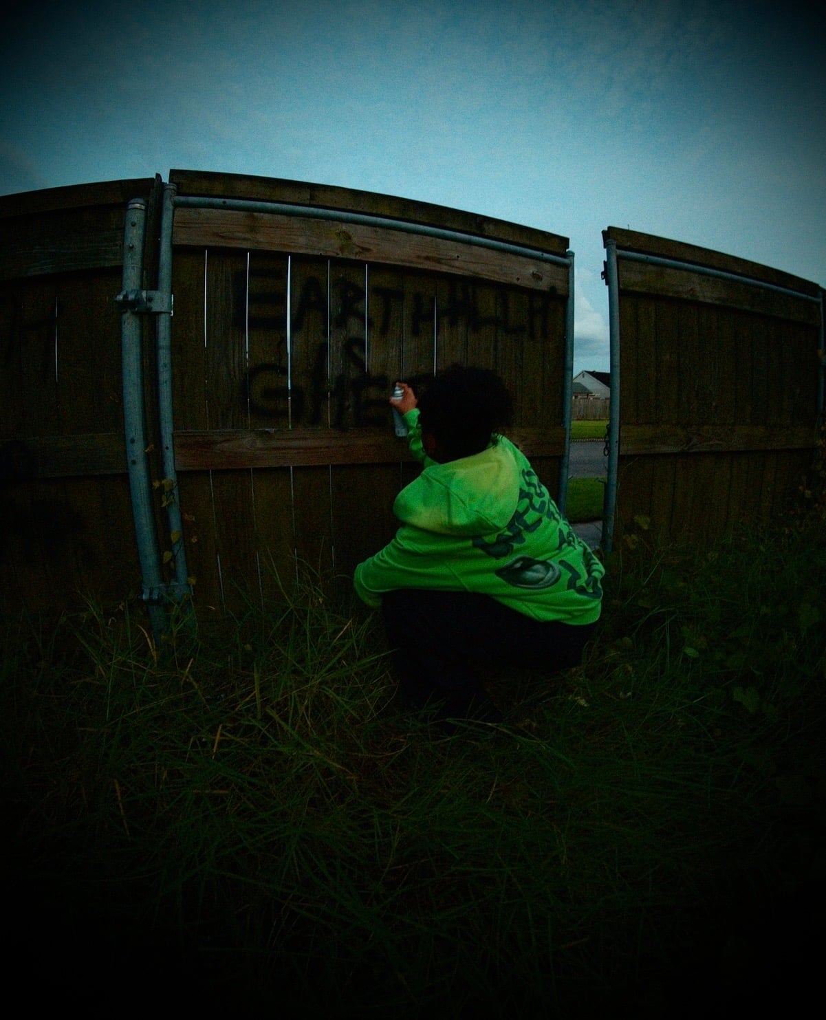 Campaign imagery: a person crouched spraying a fence, seen from behind in a neon-green hoodie with an alien and UFO print.