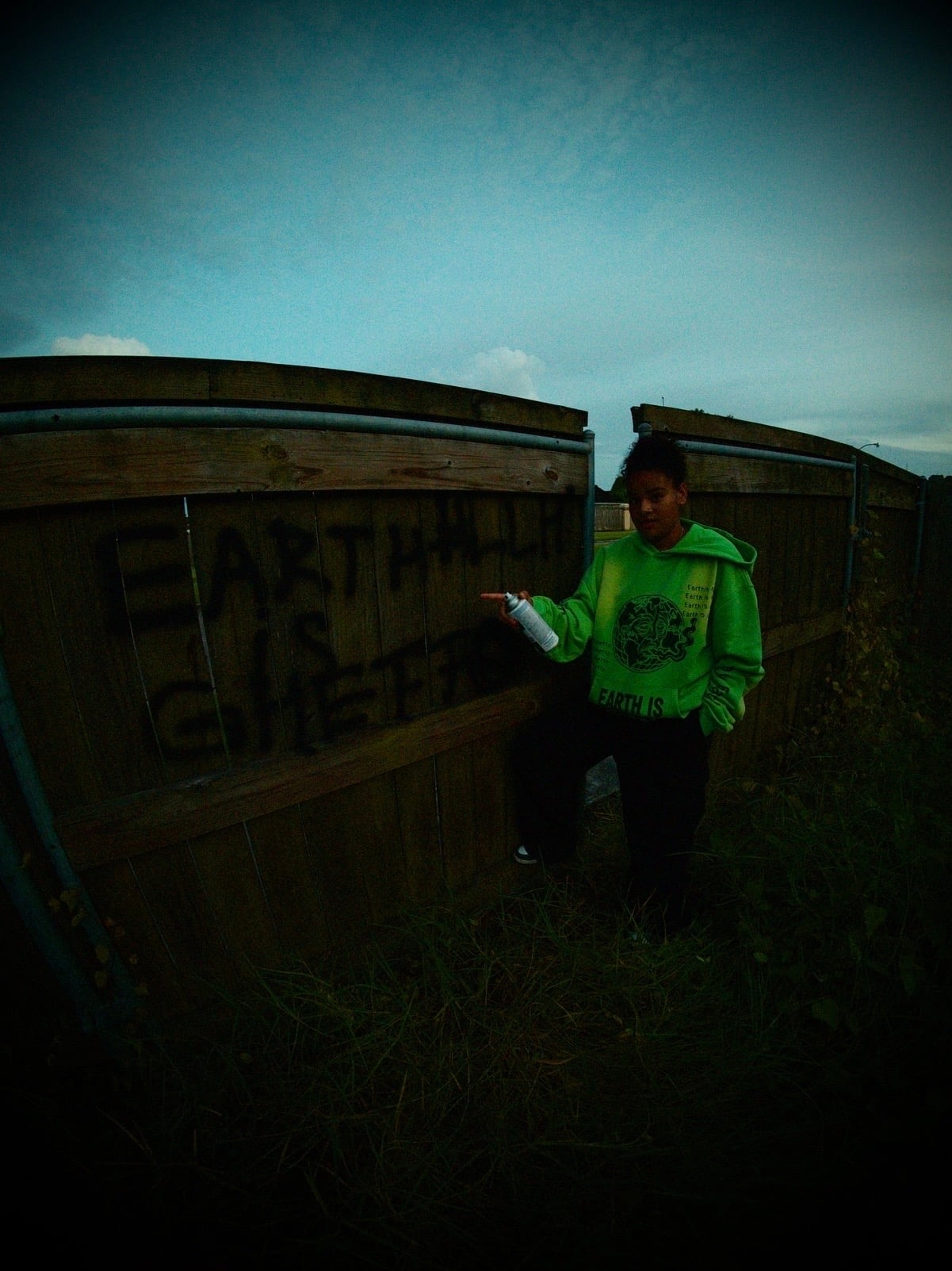 Campaign imagery: a person in a neon-green Earth Is Ghetto hoodie pointing a spray can at a graffitied fence.